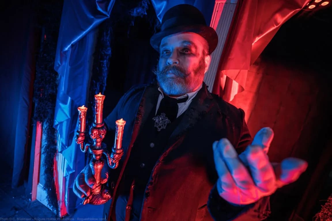 A haunted house actor dressed in a suit and holding a candle stick.