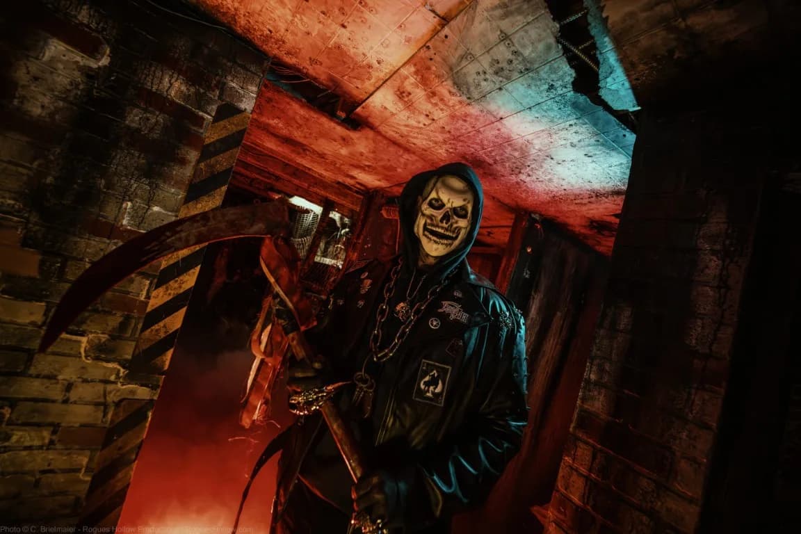 A haunted house actor dressed as a skeleton holding a scythe.
