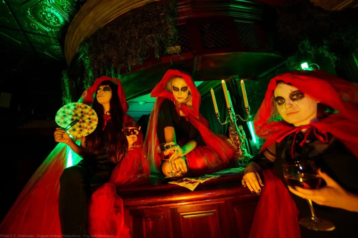 Three haunted house actors sitting around a bar and drinking red wine.
