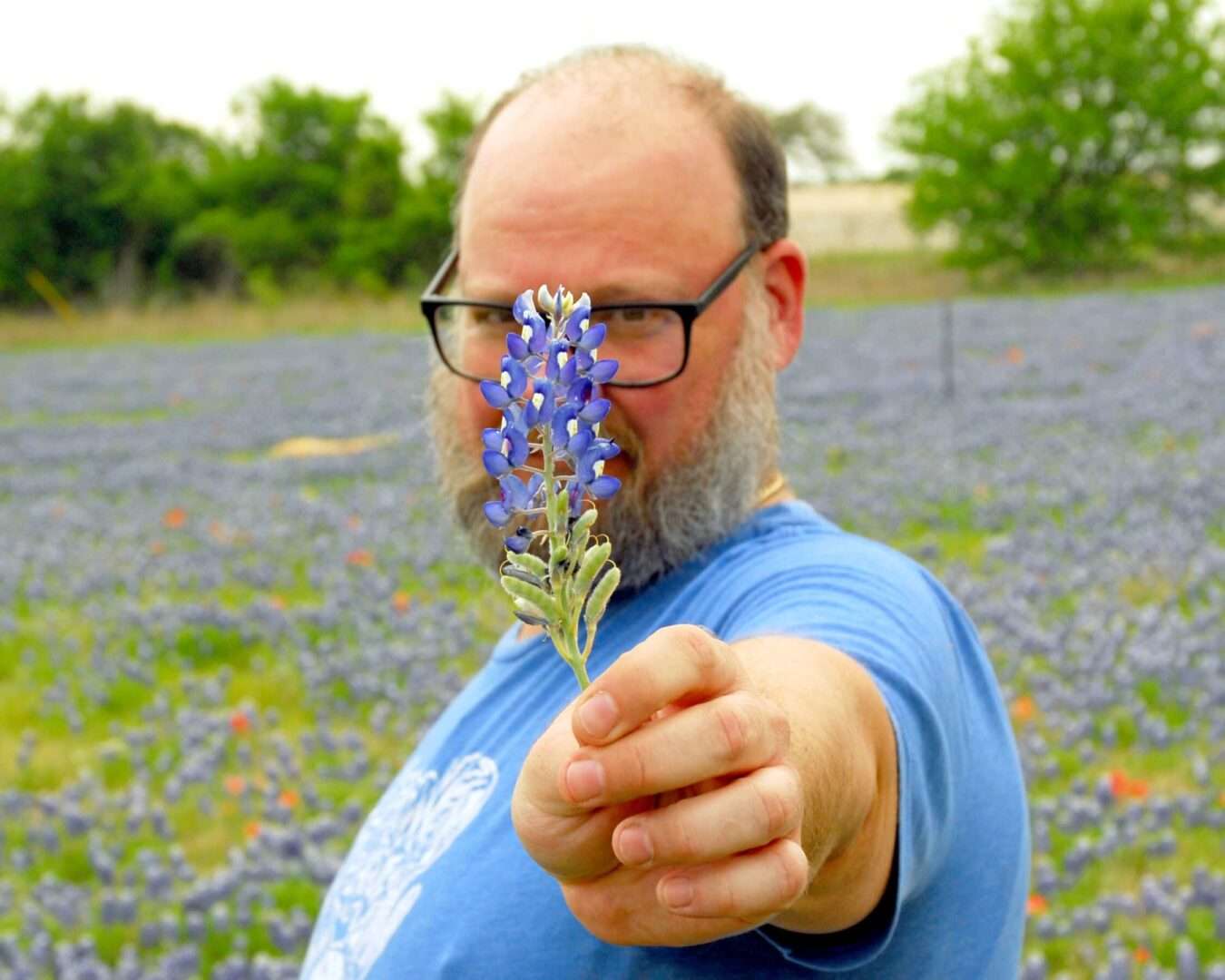 A man holding up a blue flower to the camera.